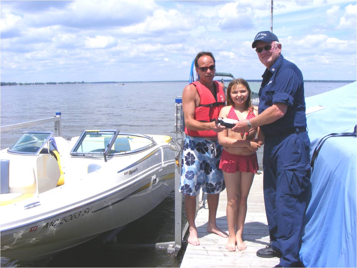 Man IN Coast Guard Auxiliary Uniform  talking to a man and a young girl both in bathing suits on a dock  with a boat next  to the dock 
