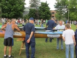 Two persons standing next to some racing canoes in a field There are several persons standing around the Canoes presumed to be racers